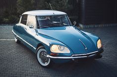 an old blue and white car is parked on the brick road in front of a house