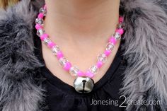 a woman wearing a pink and silver beaded necklace with a bell charm on it