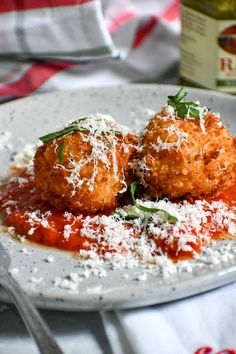 two meatballs covered in marinara sauce and parmesan cheese on a white plate