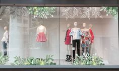 a window display with mannequins dressed in different outfits and plants behind them