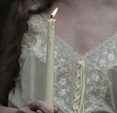 a woman holding a lit candle in her right hand and wearing a white dress with lace on it