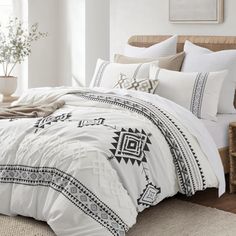 a bed with white comforter and pillows in a room next to a plant on the floor