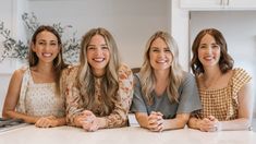 three women sitting at a kitchen counter smiling for the camera with their hands on her knees