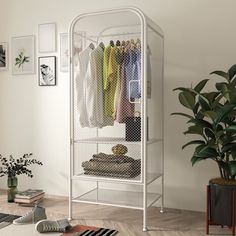 a white metal closet with clothes hanging on the rack and potted plant next to it