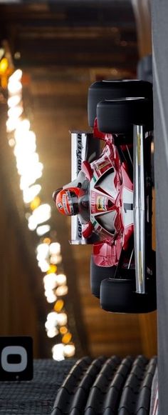 a red race car driving down a track with lights in the backgrouund