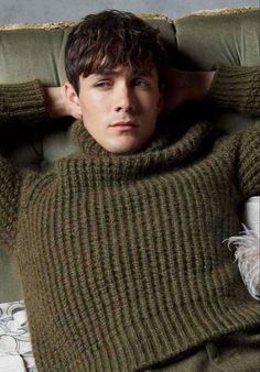 a young man laying on top of a couch wearing a green sweater and white gloves