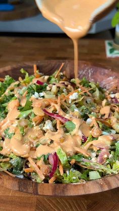 a wooden bowl filled with salad and dressing being drizzled on top of it