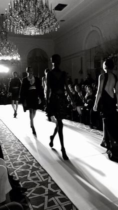 several models walk down the runway in black and white, with chandeliers hanging from the ceiling