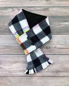 the black and white checkered scarf is laying on top of a wooden table with a button