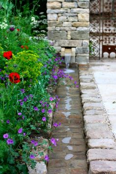 a garden with red and purple flowers next to a stone wall