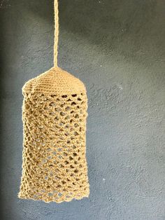 a crocheted bell hanging from a rope on a gray wall next to a vase