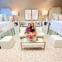 two women are sitting in the middle of a room with white furniture and pink walls