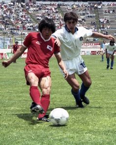 two young men playing soccer on a field in front of an audience at a stadium