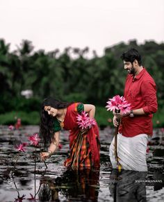 two people standing in the water with pink flowers