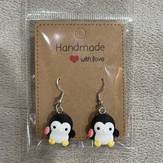 the penguin earrings are in plastic packaging on the carpet, with a tag attached to it that says handmade with love