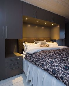 a bed sitting under a window next to a wall mounted cabinet in a bedroom on top of a wooden floor