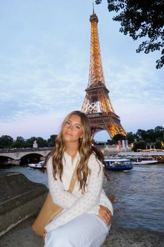 a woman sitting on the ground in front of the eiffel tower at dusk