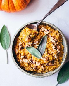 a bowl filled with food next to two pumpkins on top of a white table