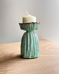 a teal colored candle holder sitting on top of a wooden table next to a white wall