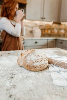 a woman standing in a kitchen next to a counter top with a loaf of bread on it