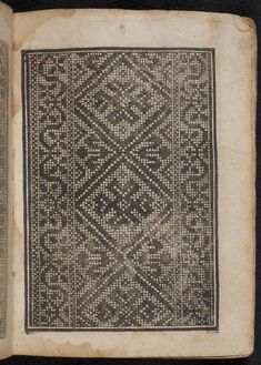 an old book with some black and white designs on the pages, in front of a black background