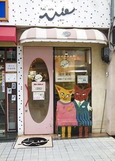 a store front with two cats painted on the doors and one cat sitting in the doorway