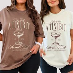 two women standing next to each other wearing matching t - shirts that say attin bit and drink club