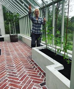 a woman standing in a greenhouse with her hands up and plants growing out of the ground