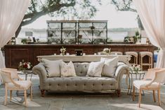 a couch and some chairs in front of a table with white drapes on it