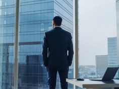 a man standing in front of a window looking out at the cityscape and skyscrapers