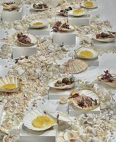 many plates and bowls filled with food on top of a white table covered in shells