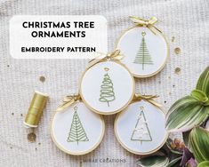 three embroidered christmas tree ornaments on a table with spools of thread next to them