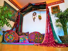 a bed covered in lots of colorful blankets and pillows next to a potted plant