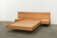 a wooden bed frame sitting on top of a cement floor next to a white wall