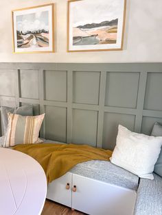 a white day bed sitting next to a table with two pictures on the wall above it