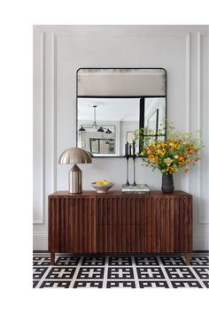 a room with a table, mirror and flowers on the sideboard in front of it