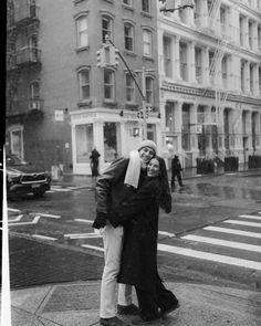 a man and woman standing on the sidewalk in front of a crosswalk with an umbrella over their heads