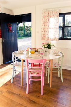 a table and chairs in a room with wood flooring, white walls and black doors