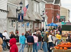 a crowd of people walking down a street next to tall brick buildings with american flags on them