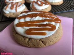 some cookies with white frosting and caramel drizzled on top are sitting on a pink plate