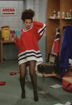 a woman in a red sweater and black stockings is holding a blue mirror while standing in a room full of clothes