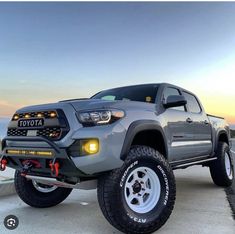 a gray toyota truck parked on top of a parking lot next to the ocean at sunset