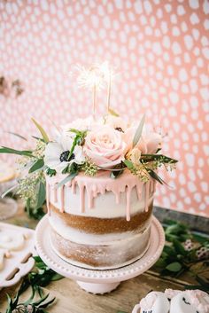 a white cake with pink icing and flowers sitting on top of a wooden table