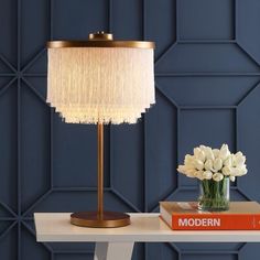 a table with a lamp and some books on it next to a vase with flowers