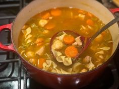 a red pot filled with pasta and carrots on top of a stovetop next to a wooden spoon