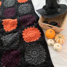 a crocheted blanket with pumpkins and a black hat sitting on top of it