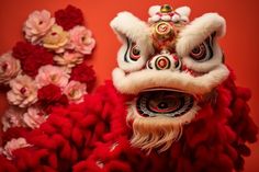 two red and white lion heads with flowers in the background, one is wearing a headdress