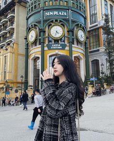 a woman standing in front of a building with a clock on it's face