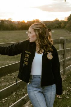 a woman leaning against a fence with her hand on the back of her jacket,