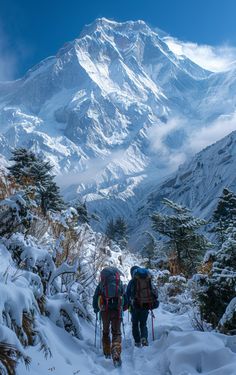 two hikers trekking up a snowy path towards a snow covered mountain range in the distance